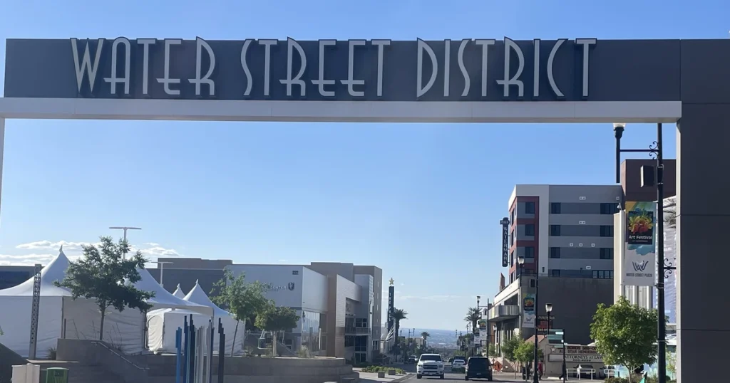 Arco de entrada al Water Street District en Henderson, con la calle y sus edificios bajo un cielo azul; foto de abril de 2024.